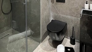 Un baño moderno con cabina de ducha de vidrio, un inodoro negro, una toalla blanca y un revestimiento de pared de mármol.