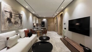 Una sala de estar moderna con un sofá, una mesa de centro y un televisor. Hay una zona de comedor con sillas y una mesa. Se observa una cocina al fondo.