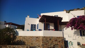 Un bâtiment blanc avec des volets bleus, un mur en pierre et un balcon agrémenté de chaises bleues.