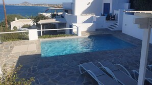 Un bâtiment moderne de couleur blanche, doté d’une piscine, d’un espace extérieur aménagé et offrant une vue sur la mer.