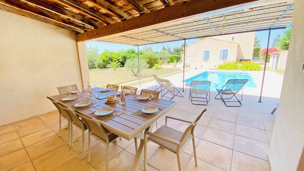 Zona d'esmorzar a l'aire lliure amb una taula ben posada per a sis persones, cadires i vistes a una piscina i vegetació.