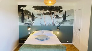 Un dormitori amb un llit, una manta verda, un mural a la paret i dues làmpades penjades a la paret.