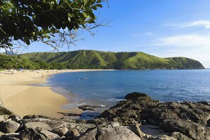 Une plage avec un rivage rocheux, une eau d’un bleu limpide et des collines verdoyantes en arrière-plan.