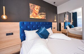 Una habitación de hotel moderna con una cama grande, una mesita de noche de madera, un espejo y una obra de arte en la pared.