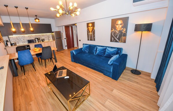 Una sala de estar moderna con un sofá azul, una mesa de centro y un comedor con sillas y una computadora portátil.
