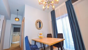 Een eetruimte met een houten tafel, blauwe stoelen, een kroonluchter, een spiegel en een uitzicht op de omgeving door grote ramen.