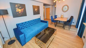 Een moderne woonkamer met een blauwe bank, een glazen salontafel en een eethoek met een houten tafel en stoelen.