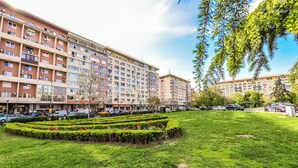 Um edifício residencial com vários andares e um pátio central com sebes bem cuidadas e um gramado.
