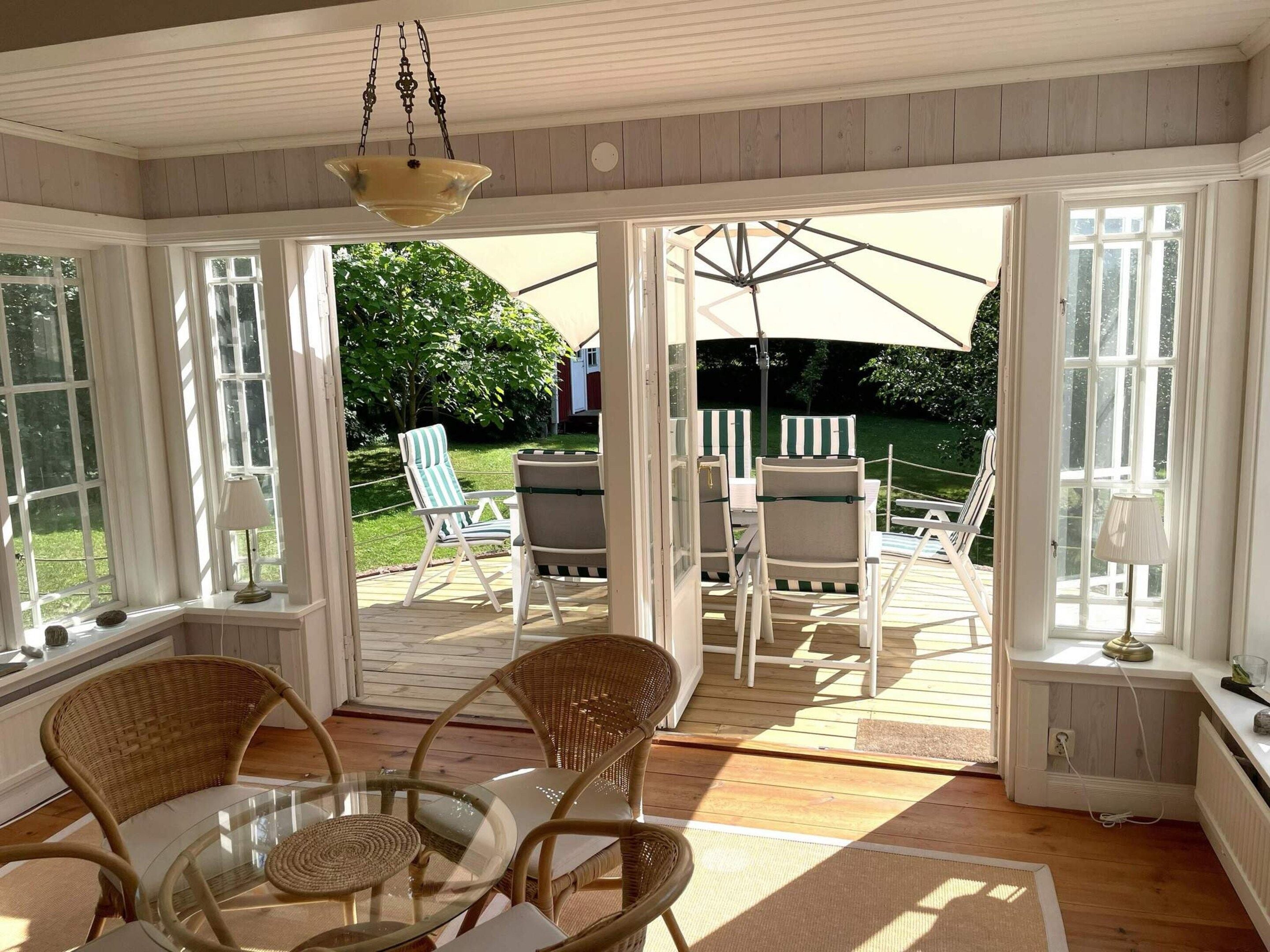 A room with a glass table and wicker chairs, large windows, and a view of the outdoors.