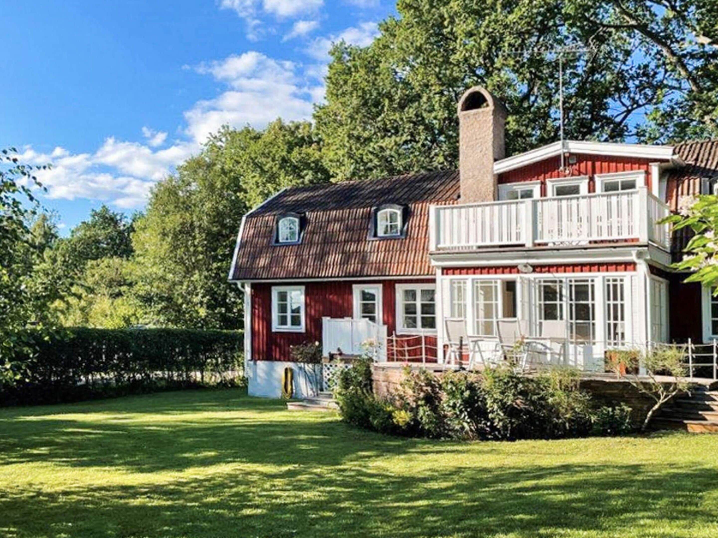 A two-story house with a red exterior and white trim, a chimney, and a balcony.