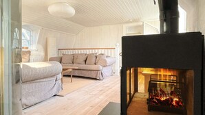 A cozy living room with a modern sofa, a small table, and a wood-burning stove. - 4 Star Holiday Home in Farjestaden (Farjestaden)
