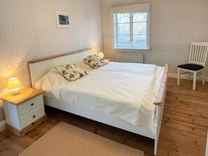 A bedroom with a bed, a nightstand, a chair, a window, and a picture on the wall. - 4 Star Holiday Home in Farjestaden (Farjestaden)