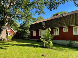 A red building with a sloped roof, surrounded by green grass and trees. - 4 Star Holiday Home in Farjestaden (Farjestaden)