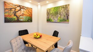 A dining area with a wooden table, four grey upholstered chairs, and two paintings on the walls.