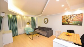A modern living room with a sofa, a dining table with fruit, a painting, and a clock on the wall.