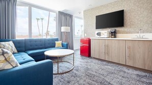 A hotel room with a blue sofa, a small round table, a kitchenette with a microwave, and a TV mounted on the wall.