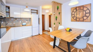 Une cuisine moderne avec des armoires blanches, un plan de travail en bois et un four encastré. On y trouve également un coin repas avec une table en bois et des chaises grises.