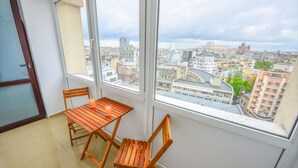 Un balcon avec une table en bois et deux chaises, donnant sur un paysage urbain composé de différents bâtiments.