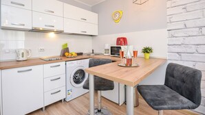 A compact kitchen with white cabinets, a wooden countertop, a washing machine, a coffee maker, and a clock on the wall. - Candy Studio - Cismigiu Gardens - Quiet Room - Open Kitchen -Smart Tv (București)