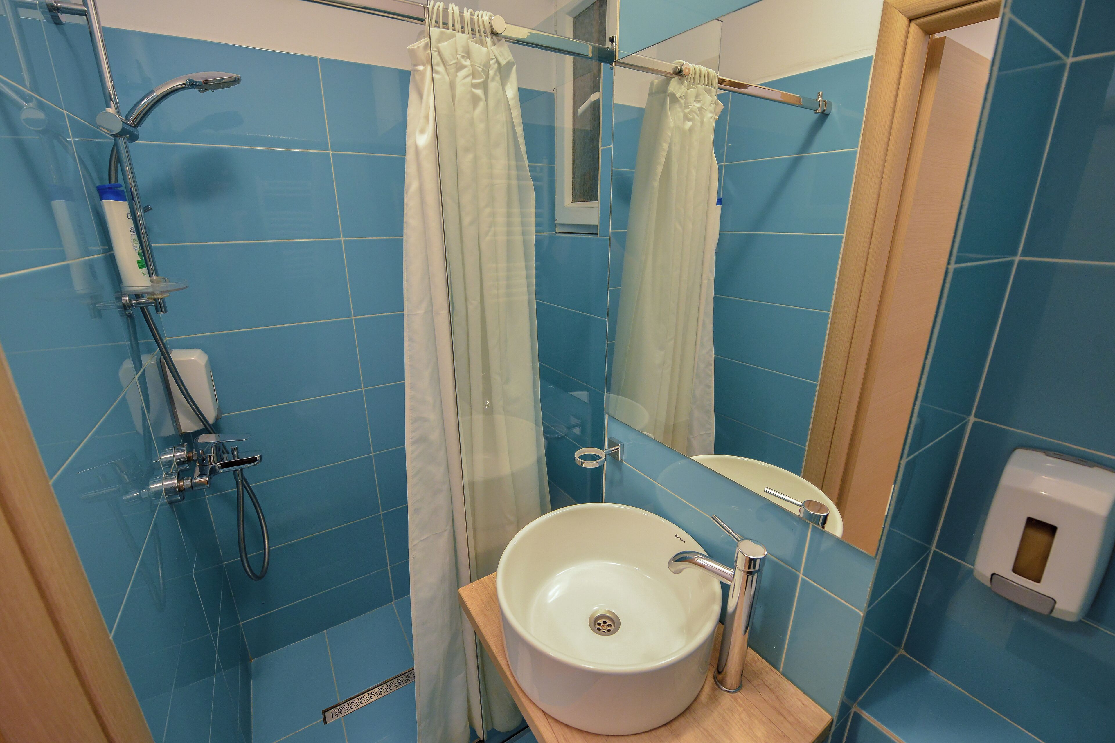 A bathroom with blue tiles, a white sink, a shower, and a mirror.