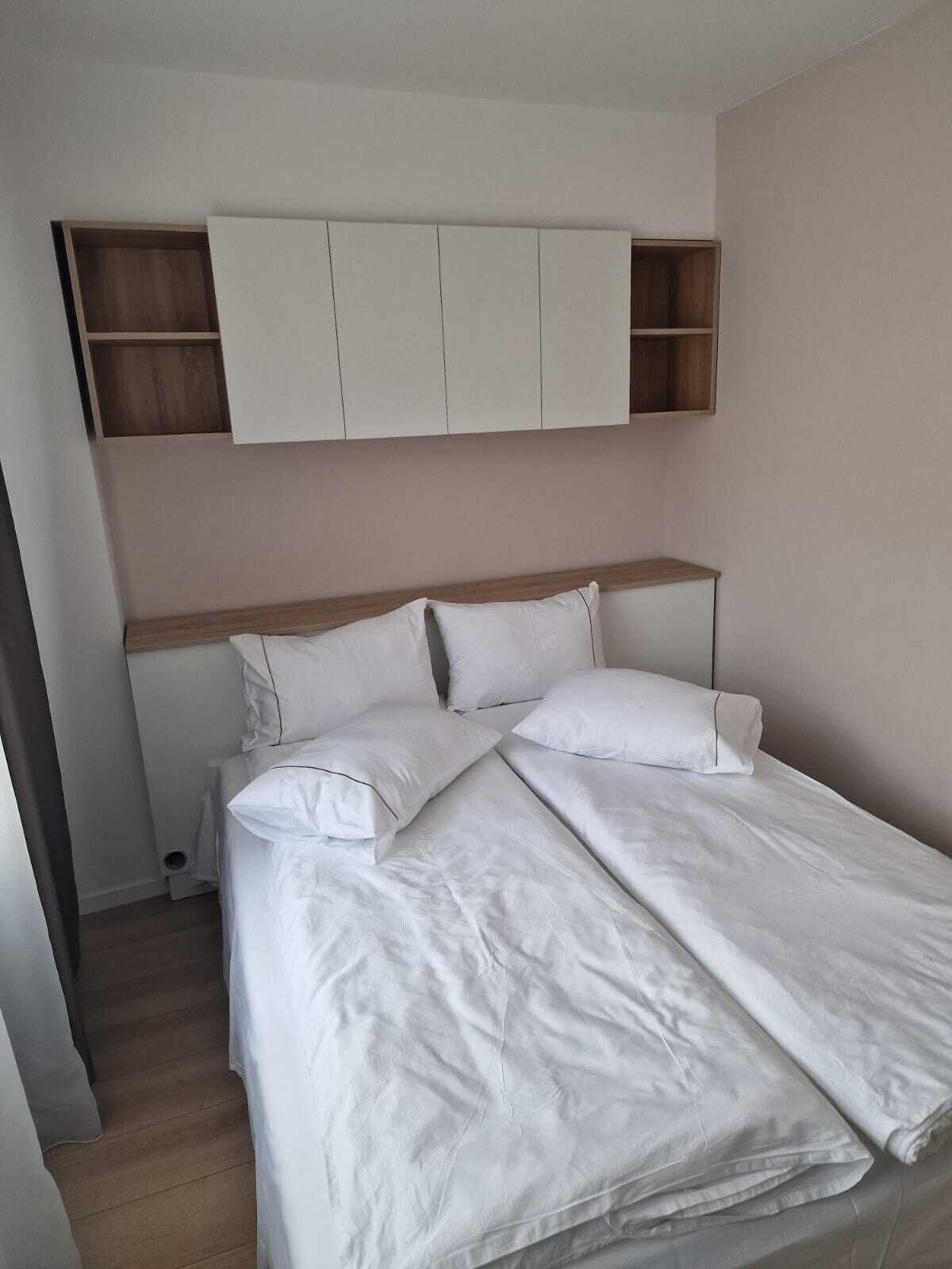 A neatly made bed with white linens in a room with a wooden headboard and built-in shelving above the bed.