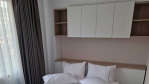 A double bed with white linens, a wooden headboard, and a built-in shelf above.