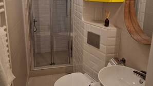 A bathroom with a glass shower enclosure, a toilet, and a sink with a yellow cabinet above.