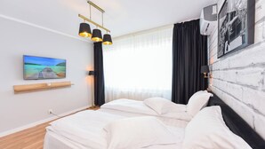 A hotel room with a bed, a mounted TV, a wall-mounted air conditioner, and a window with curtains.