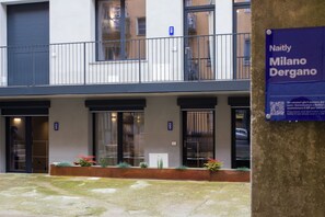A modern building with a balcony, a sign reading "Naitly Milano Dergano," and a small garden area with plants. - Naitly Milano Dergano (Milan)