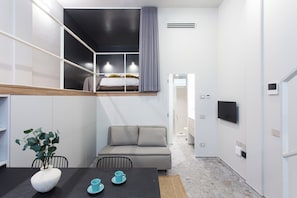A compact, modern room with a loft bed, a sofa, a dining table with a vase and cups, and a TV mounted on the wall. - Naitly Milano Dergano (Milan)