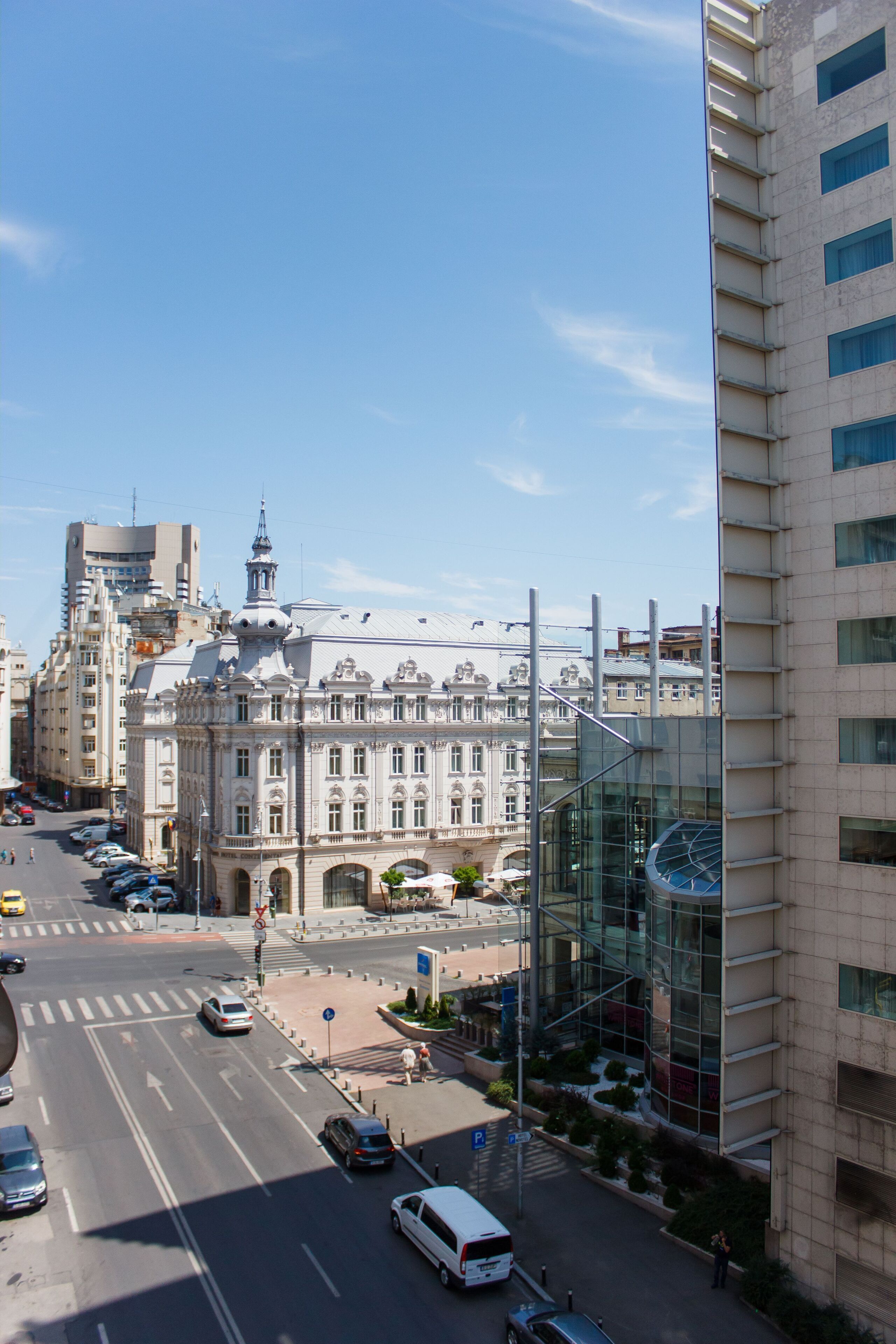 Eine Stadtstraße mit einem historischen Gebäude, einer modernen Glasarchitektur und einer Straßenbahn.