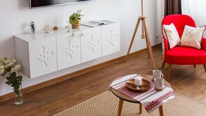 Un salon moderne avec un téléviseur à écran plat, un fauteuil rouge, une petite table avec un plateau, une lampe sur pied et une plante décorative.