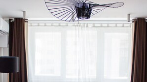 Un salon moderne avec un canapé rouge, un fauteuil rouge, une table basse ronde sur laquelle se trouvent des tasses et un plateau, ainsi qu’un luminaire noir original fixé au plafond.