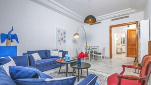 Un salon moderne avec un canapé bleu, un fauteuil rouge et un coin repas comprenant une table et des chaises.
