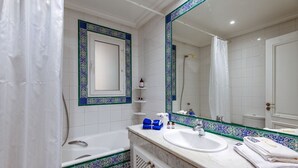 Une salle de bain avec une baignoire, un lavabo, un grand miroir et un espace douche.