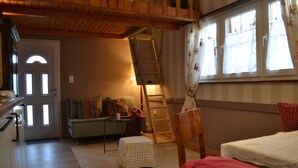 Una habitación acogedora con una escalera de madera, un sofá con cojines de colores, una mesita con lámpara y una ventana con cortinas.