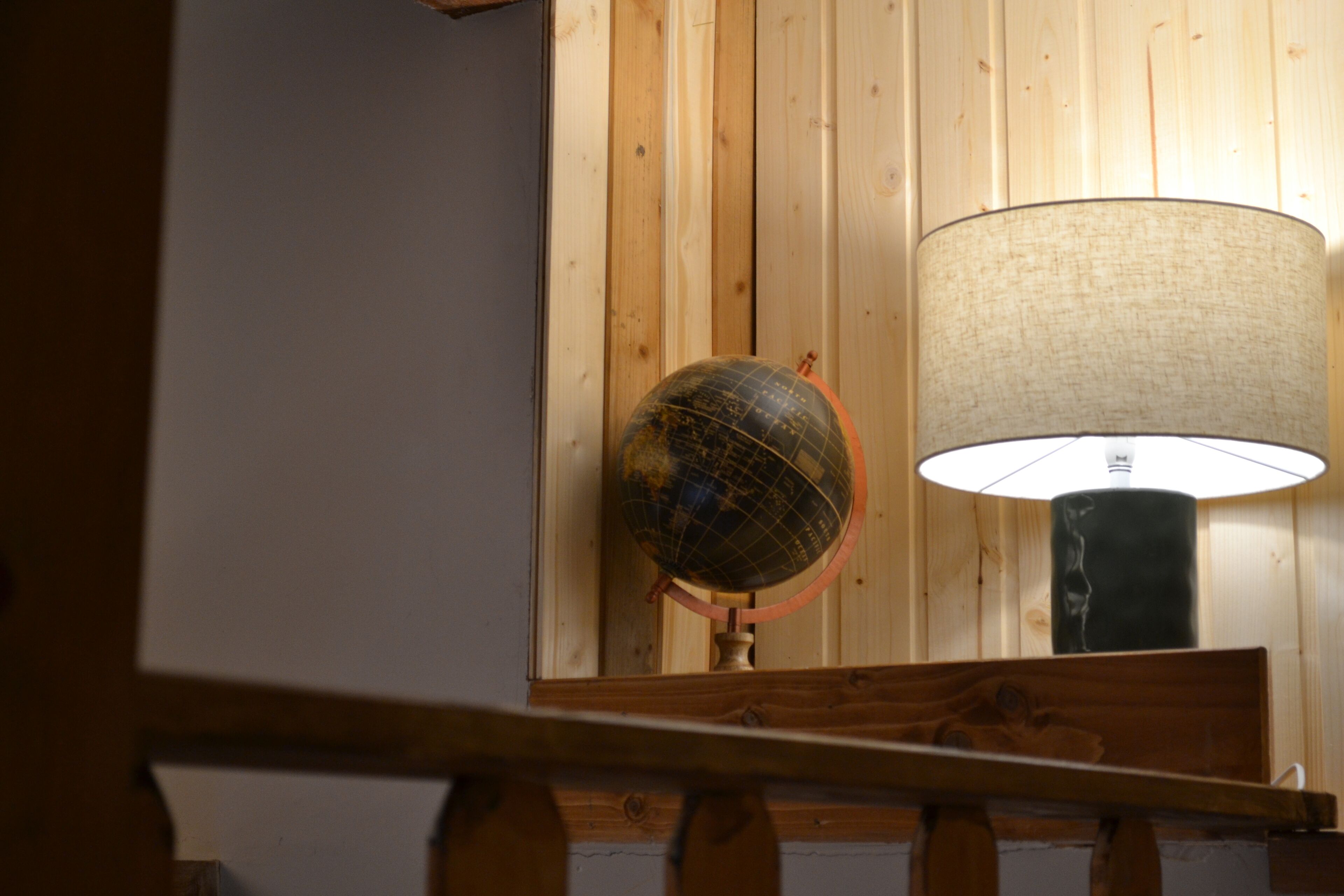 Ein Globus und eine Lampe auf einem Holztisch vor einer Holzwand.
