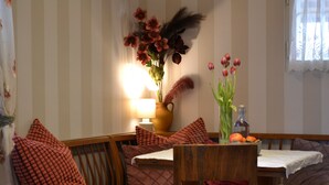 Un área de comedor con papel tapiz a rayas, una mesa de madera y un banco. Hay varios cojines y un jarrón con flores sobre el banco.