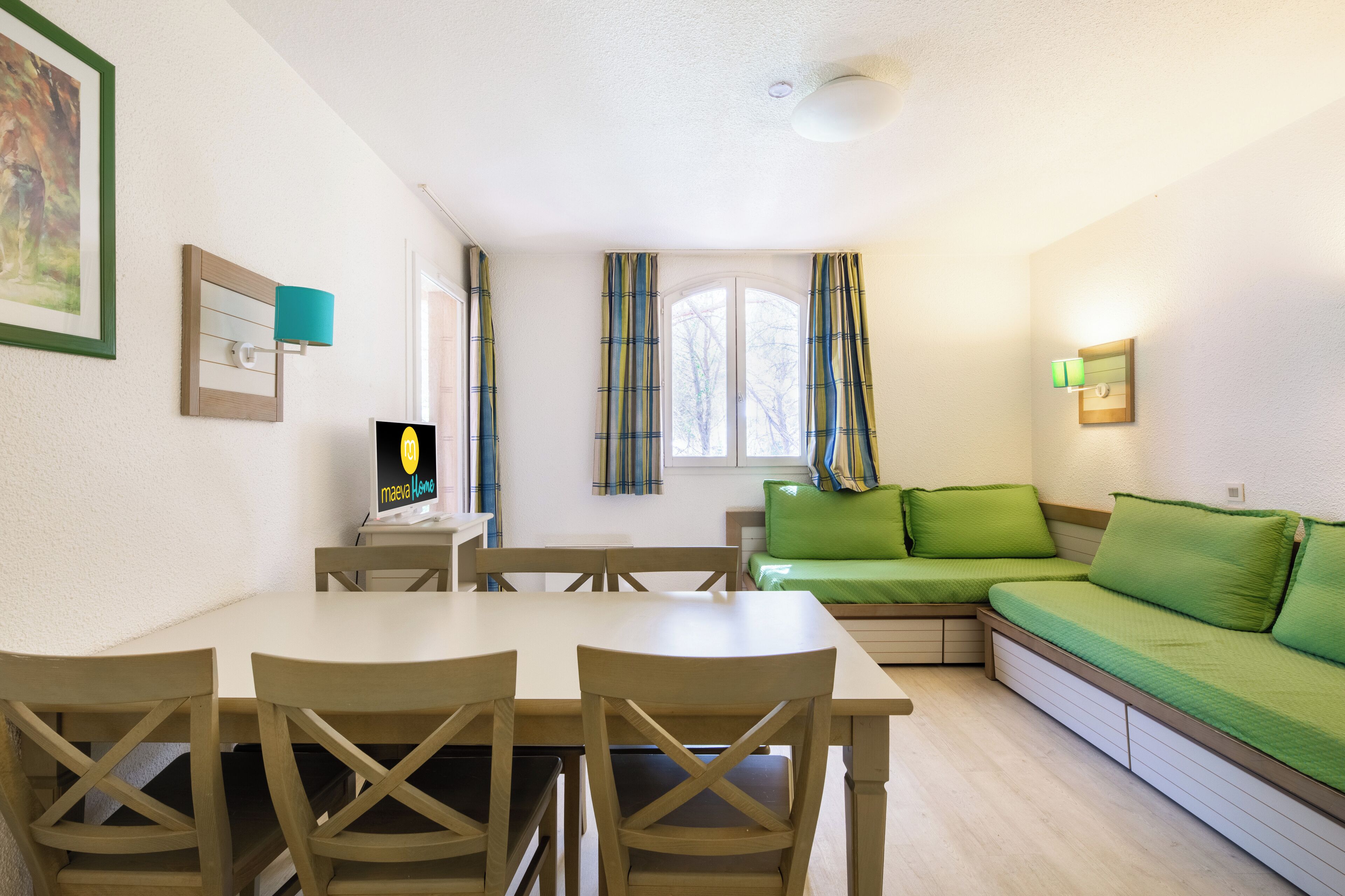 Een gezellige kamer met een eettafel, stoelen, een groene bank en een kleine televisie.