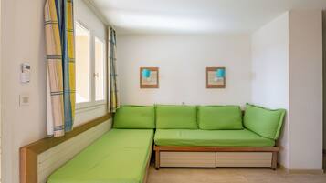 A compact room with a green sofa, a small bed, and two wall-mounted light fixtures.