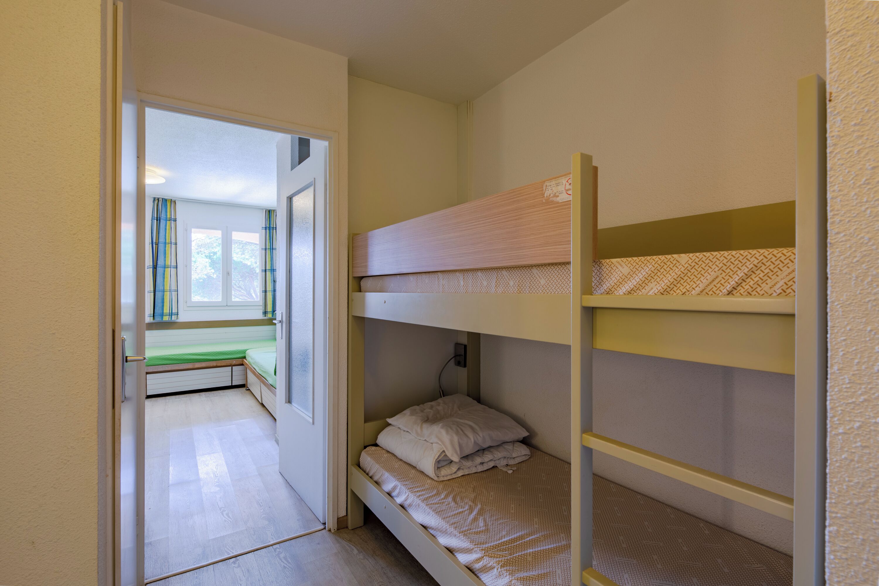 Une chambre avec un lit superposé, une fenêtre et une porte donnant sur une autre pièce.