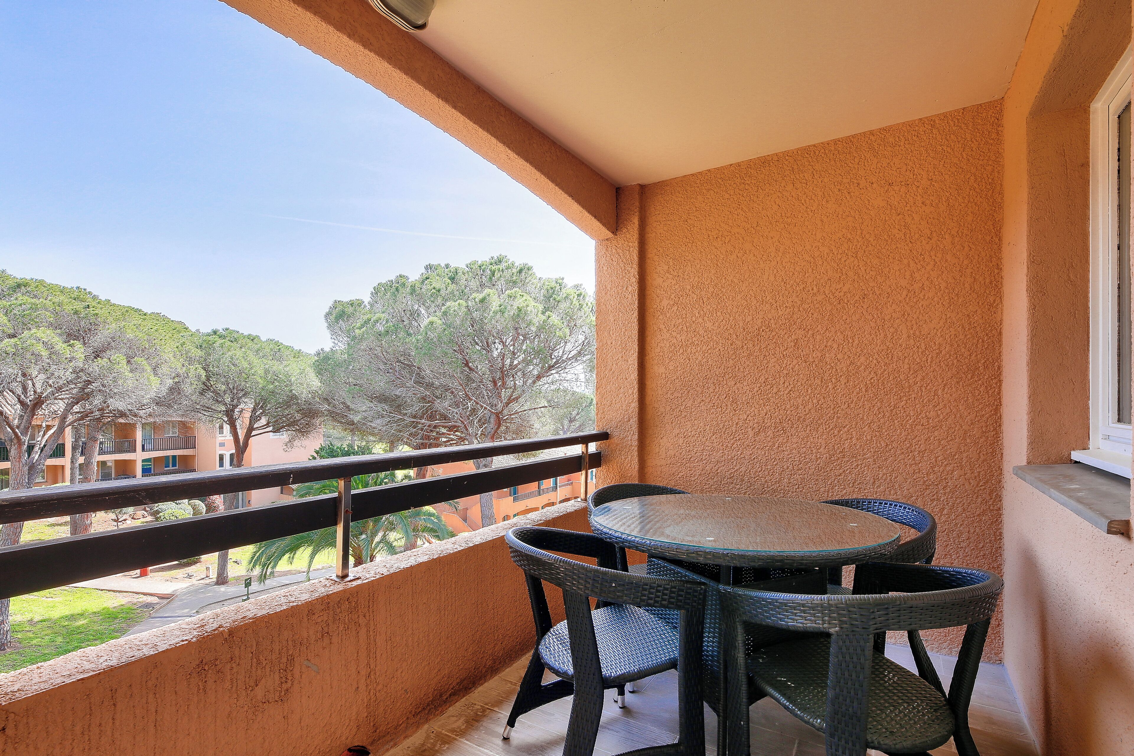 Een balkon met een ronde tafel en stoelen, uitkijkend op een binnentuin met bomen en gebouwen.