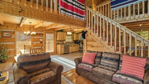 Interior rústico de una cabaña con escalera de madera, un conjunto de sofás y una zona de comedor.
