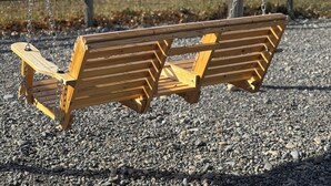 A wooden swing set with metal chains, set on a gravel surface with a wooden fence and trees in the background. - Brand New Quiet Country Cabin (Rock View County)