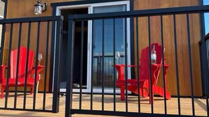 A wooden building with a black metal fence, a glass door, and red chairs outside. - Brand New Quiet Country Cabin (Rock View County)