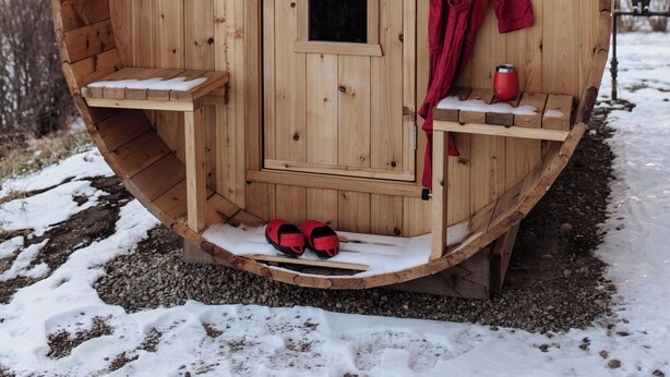 A wooden sauna with a door, a bench, a coat rack, and a pair of red shoes outside. - Brand New Quiet Country Cabin (Rock View County)