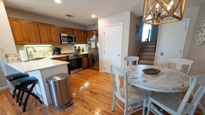 A kitchen with wooden cabinets, stainless steel appliances, a white island with stools, and a dining table with chairs.