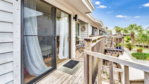 A wooden deck with a glass door leading to a room with a view of palm trees and a clear sky.