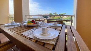 A wooden table set for two with plates, cutlery, and a bowl of fruit on a balcony with a clear view of buildings and trees. - Albufeira Sunny Style by Homing (Albufeira)