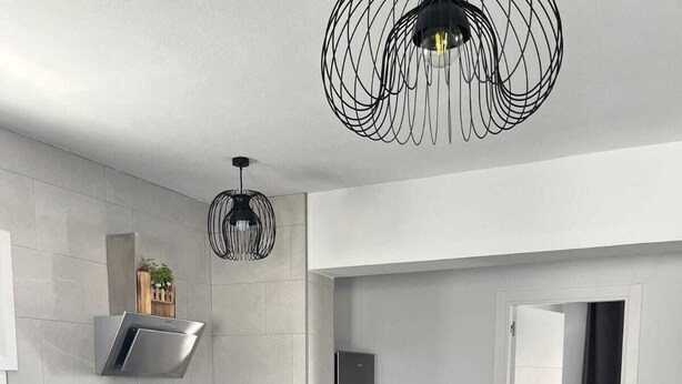 A modern kitchen with white cabinets, a black countertop, a built-in refrigerator, and a pendant light. - Terapia Salada I   . (Zahora)